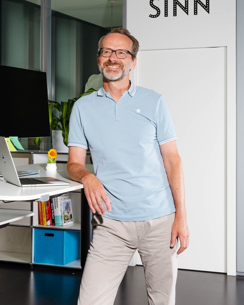 Marcel Oberhänsli stands smiling beside a standing desk with a laptop.