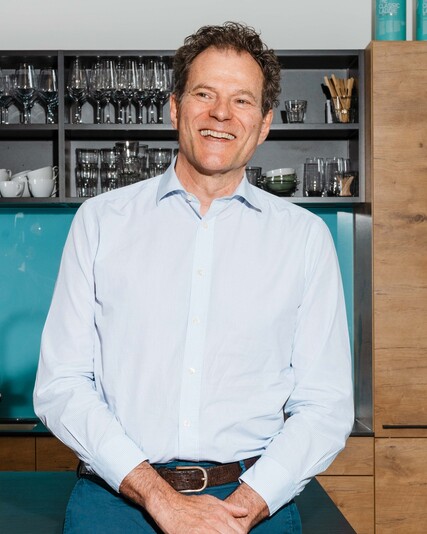 Benno Maggi stands smiling in front of the office kitchen.