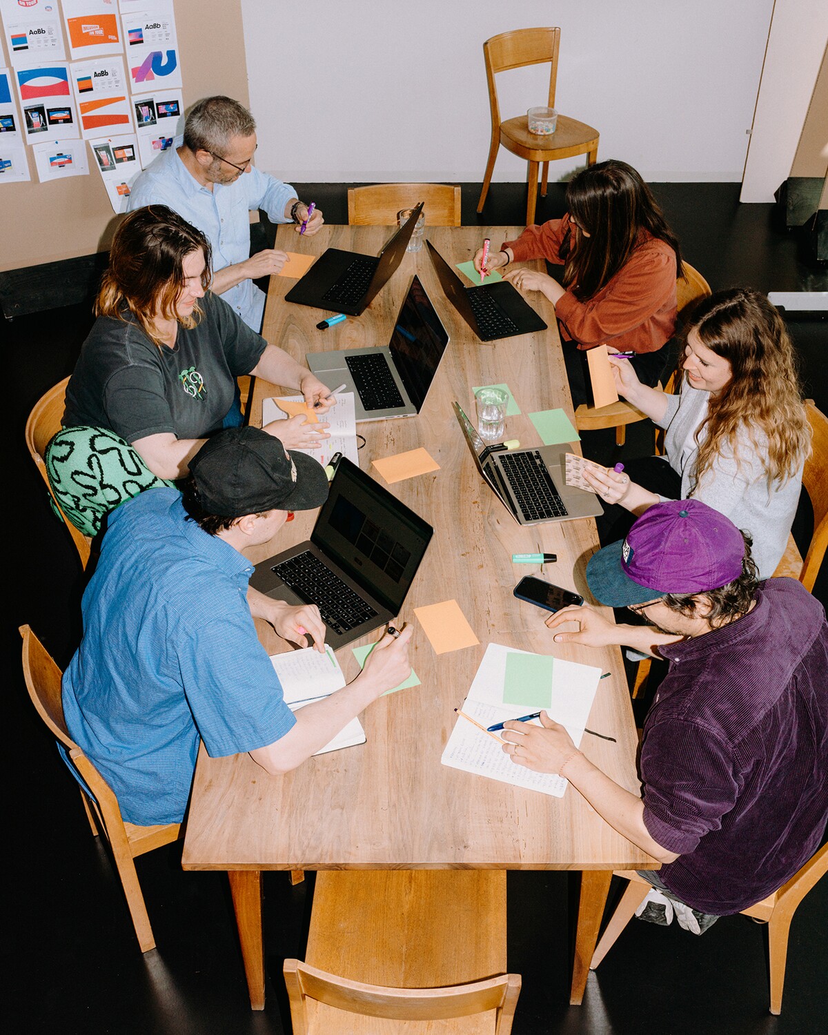 Six team members work together with laptops and notepads around a table.