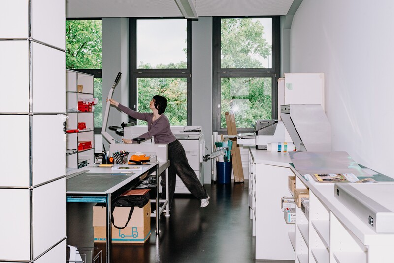 A colleague reaches towards shelving in a bright production room.
