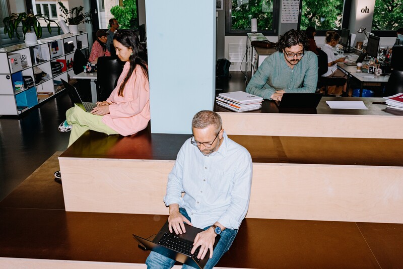 Three team members work on laptops at different levels of a tiered seating area.