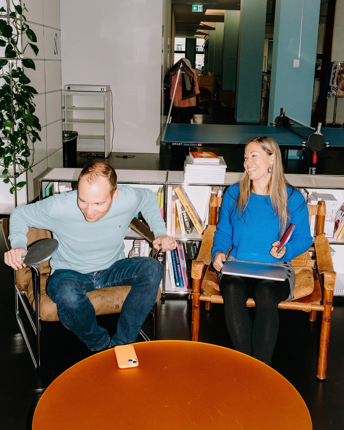 Two team members sit in armchairs holding table-tennis paddles.