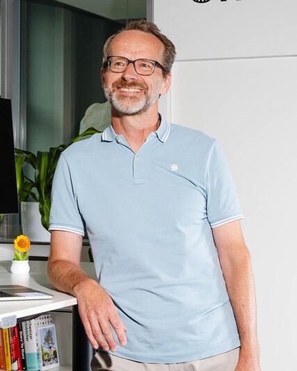 Marcel Oberhänsli stands smiling beside a standing desk with a laptop.