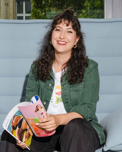 Alisa Kuratli sits on a light-blue sofa holding an open magazine.