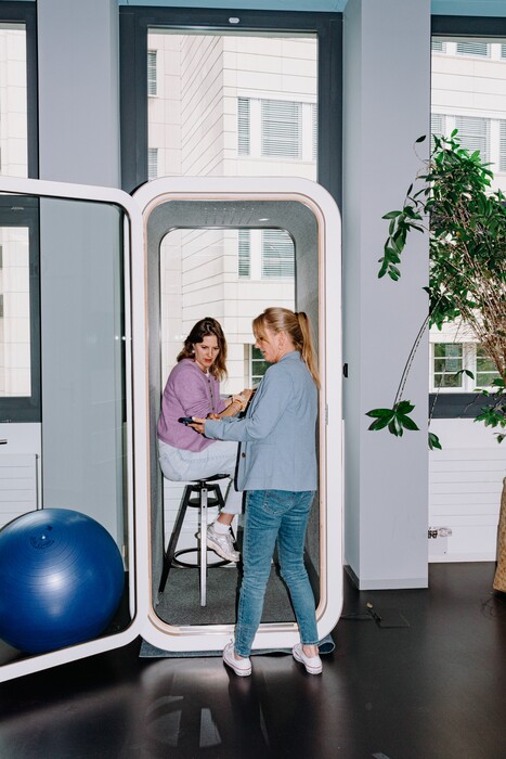 Two colleagues talk inside a glass work booth.