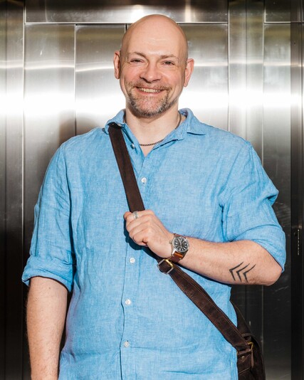 Stefan Melz stands in a lift wearing a shoulder bag.