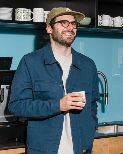 David Hauser stands in the office kitchen holding a cup.