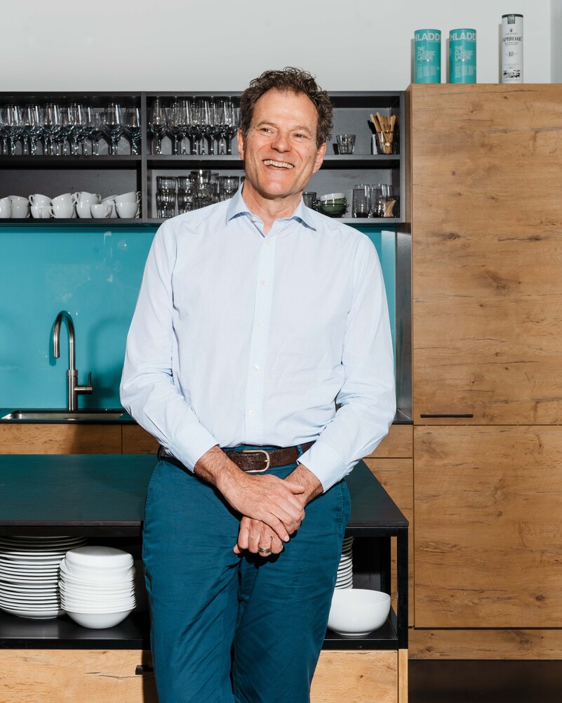 Benno Maggi stands smiling in front of the office kitchen.