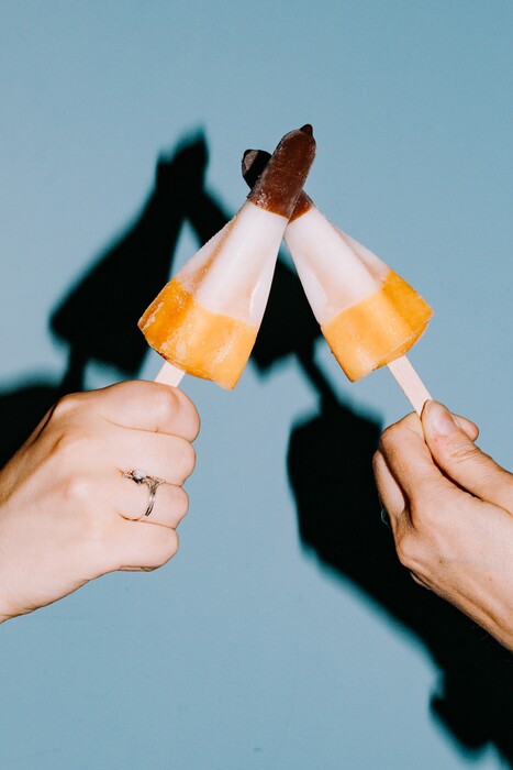 Two hands toast with multicoloured ice lollies.