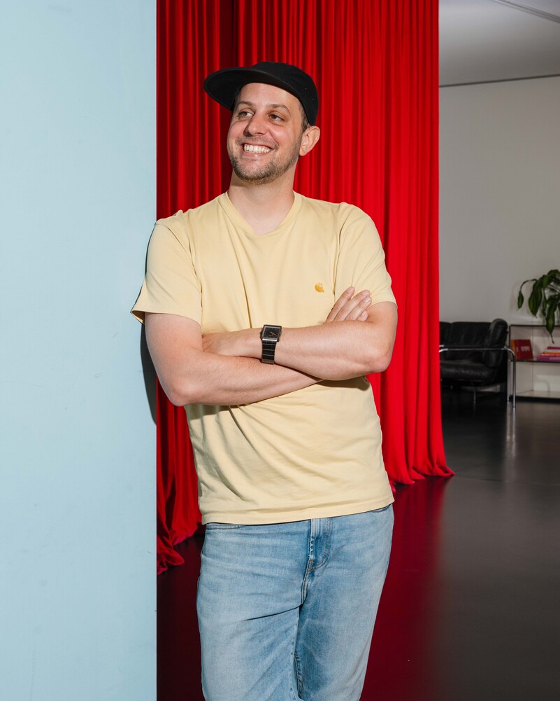 Fabian Solèr leans with his arms crossed beside a red curtain.