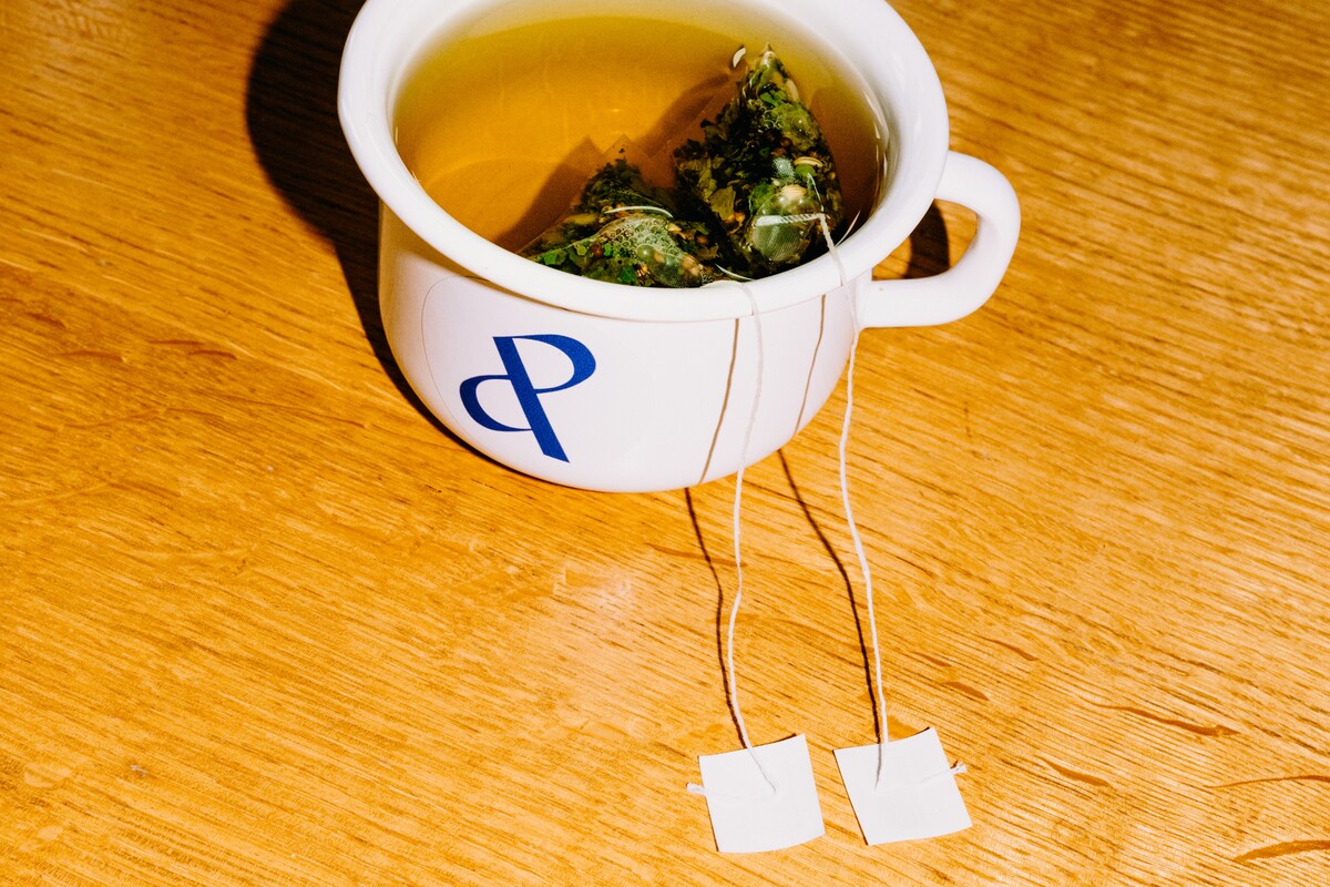 A cup bearing the company symbol contains tea and two tea bags.