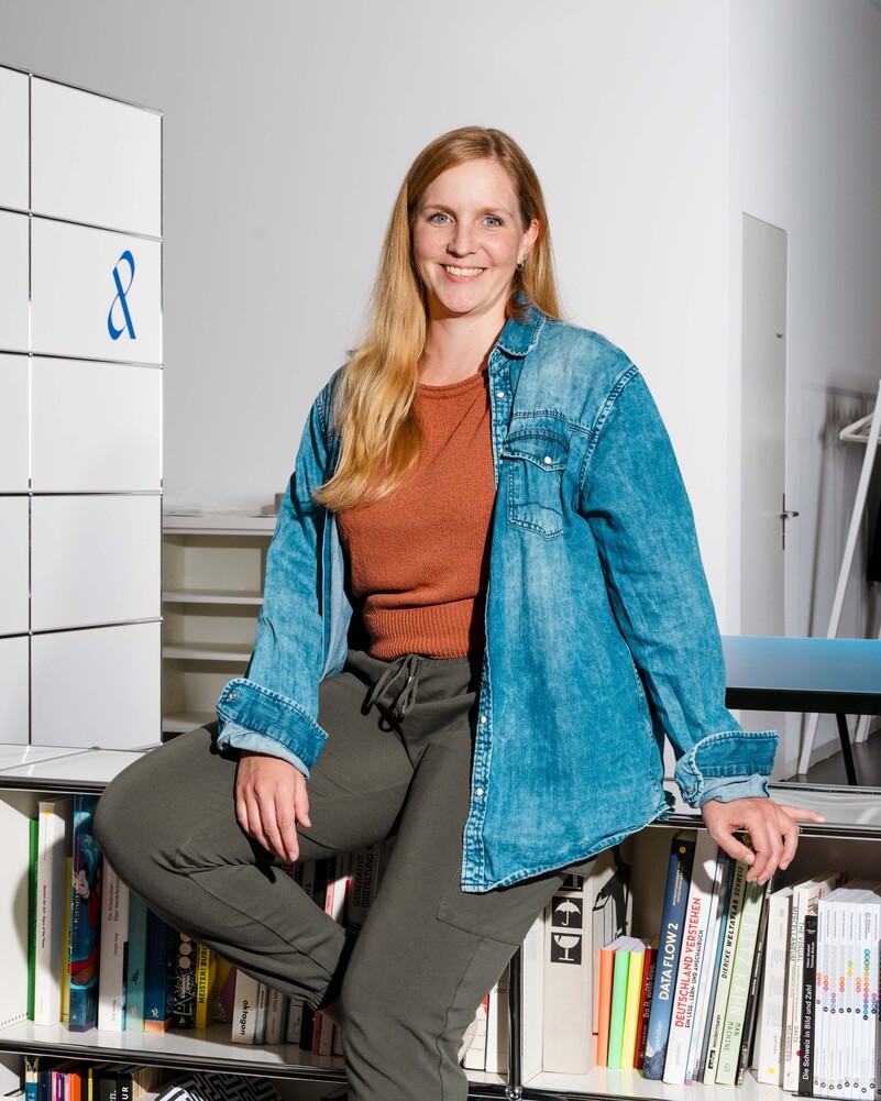 Swetlana Bregy leans smiling against a bookshelf.