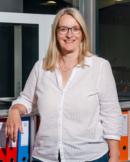 Heidi Munderich stands smiling in front of shelves filled with colourful binders.