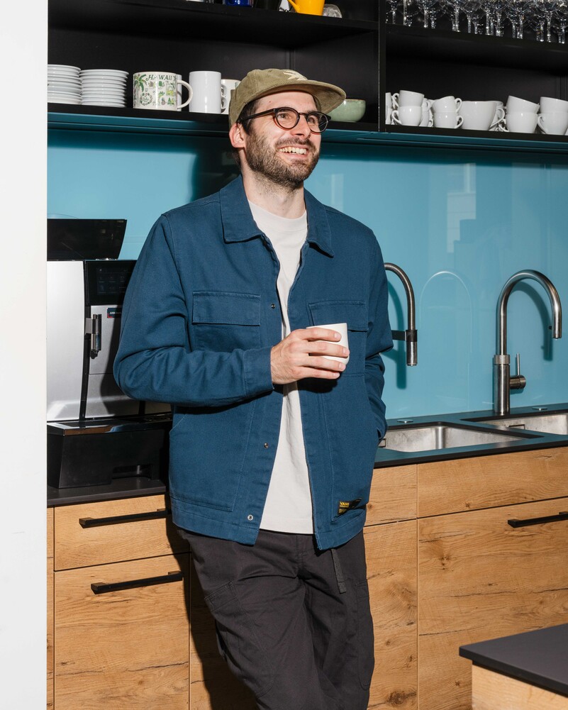 David Hauser stands in the office kitchen holding a cup.