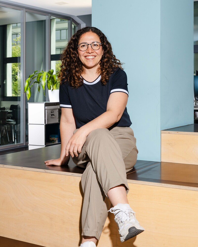 Federica Mele sits smiling on a wooden step in the office.