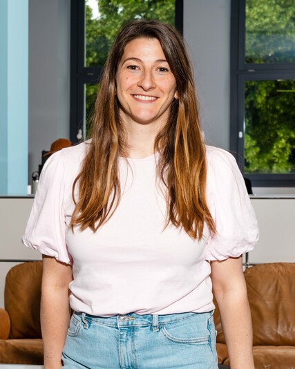 Tiziana Mascolo stands smiling in front of a brown leather sofa.