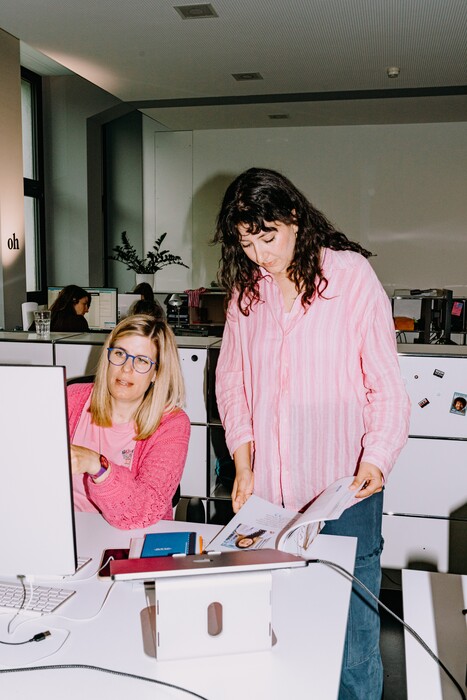 Two colleagues inspect printouts beside a large printer.