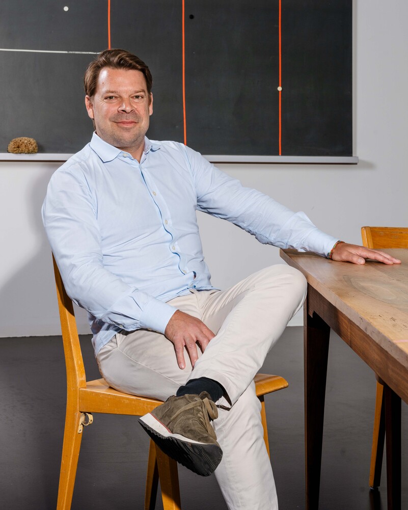 Manuel Specker sits at a wooden table with his legs crossed.