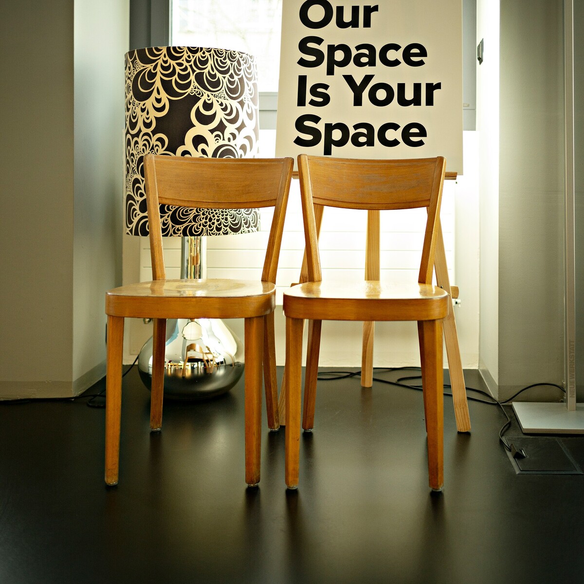 Two wooden chairs stand in front of the words “Our Space Is Your Space.”