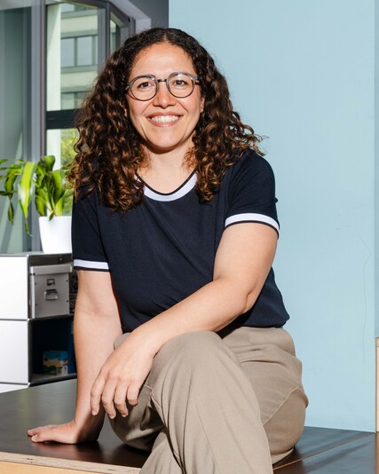 Federica Mele sits smiling on a wooden step in the office.