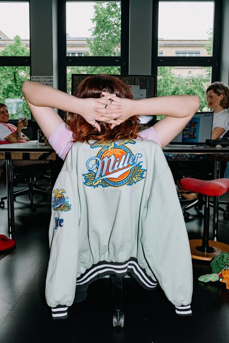 A team member leans back at a workstation with hands clasped behind their head.