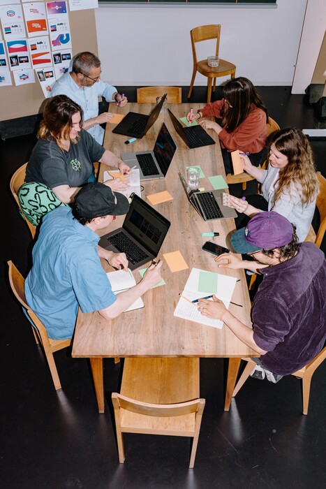 Six team members work with laptops and notepads around a wooden table.