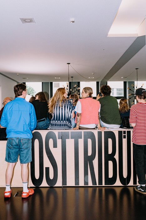 A group gathers, sitting and standing, behind a high wooden counter.