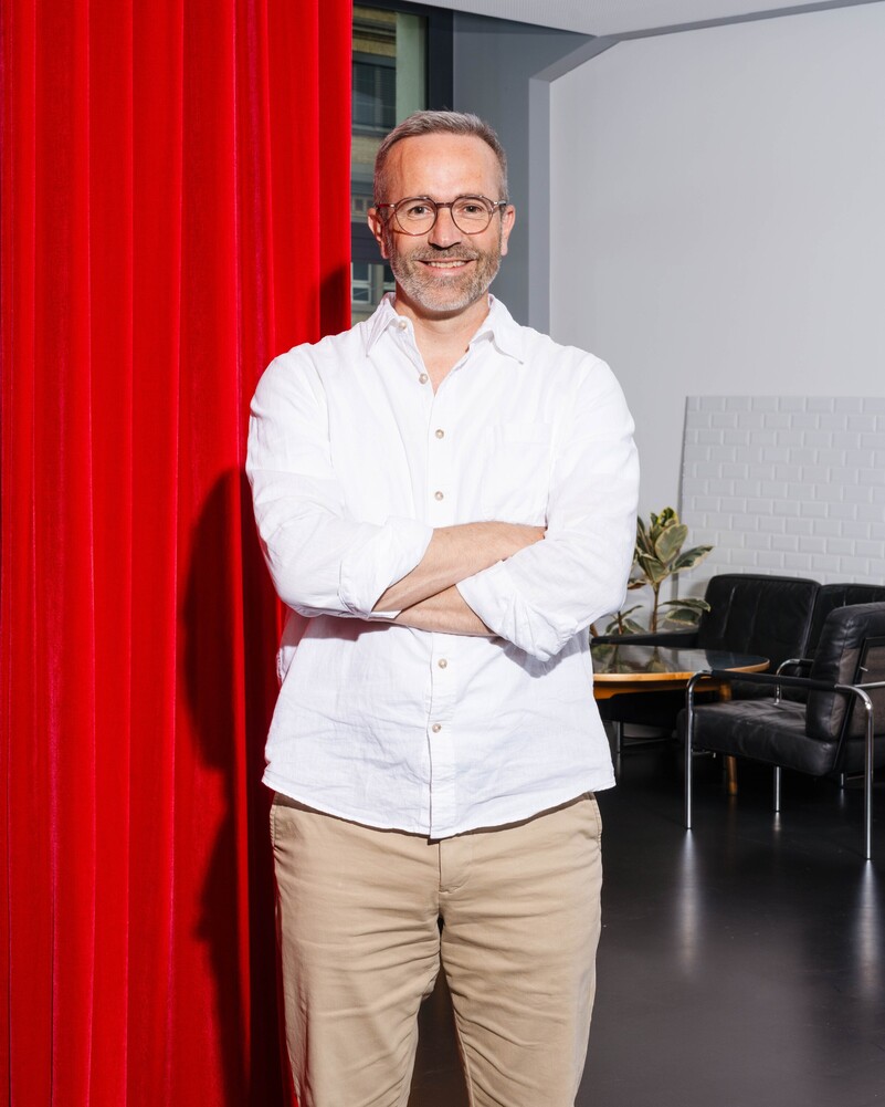 Urban Fetz stands with his arms crossed beside a red curtain.