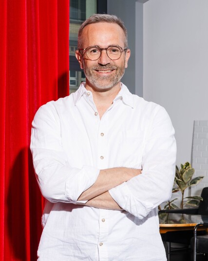 Urban Fetz stands with his arms crossed beside a red curtain.