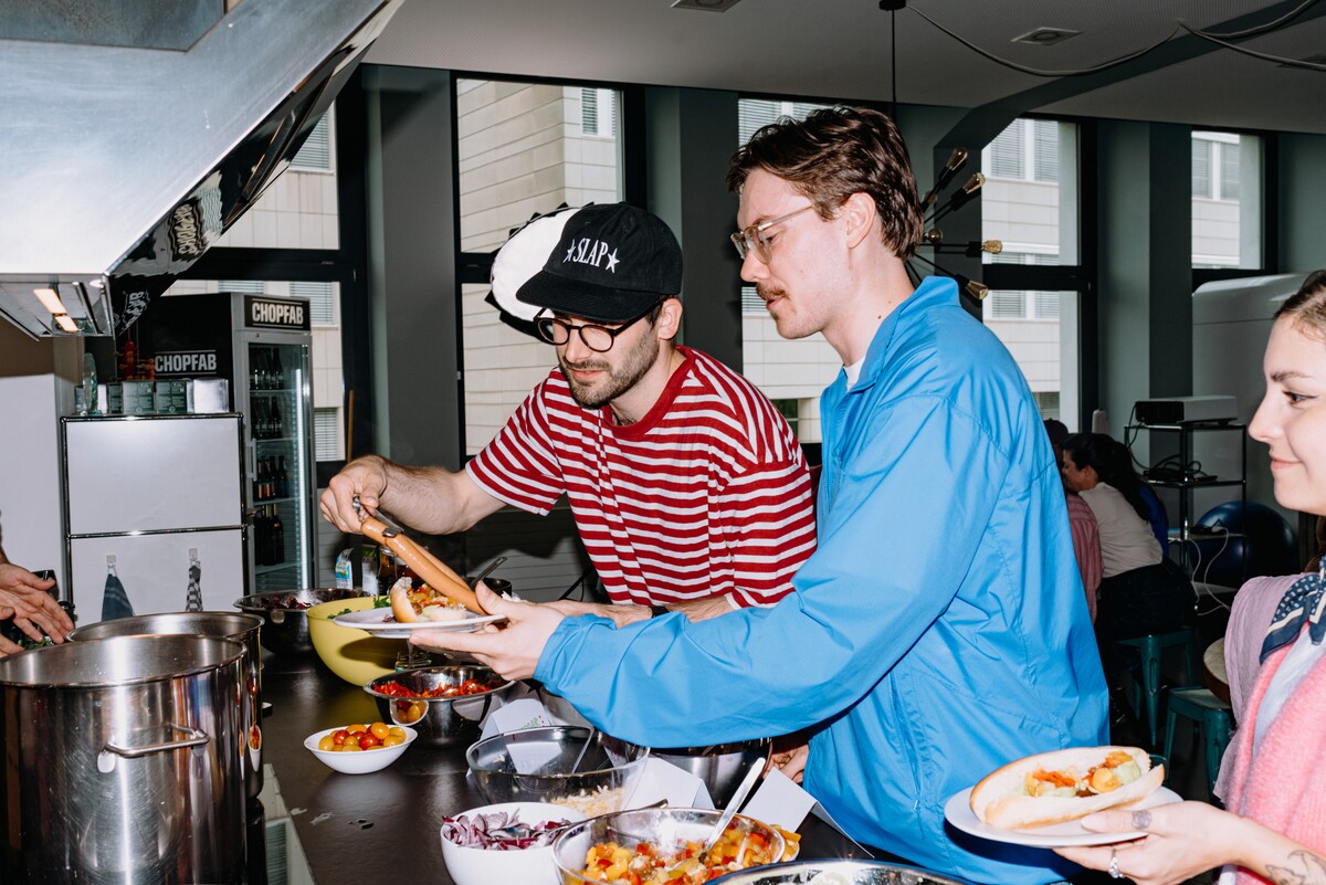 Two team members serve food from pots at a buffet.