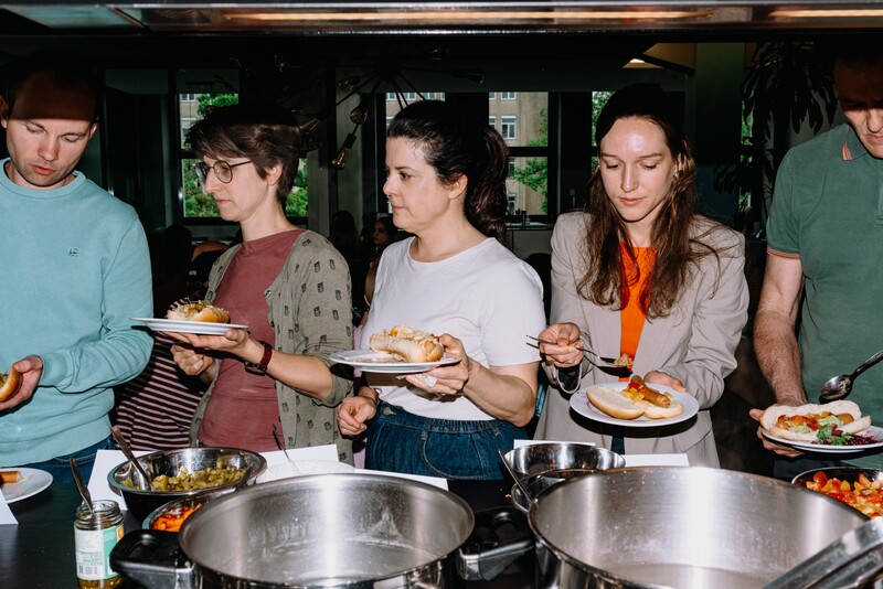 Team members serve food onto plates at a kitchen buffet.