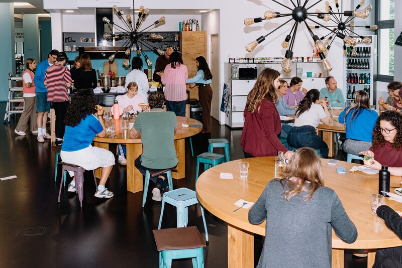 Numerous team members share a meal at round tables.