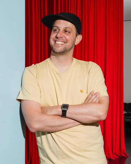 Fabian Solèr leans with his arms crossed beside a red curtain.