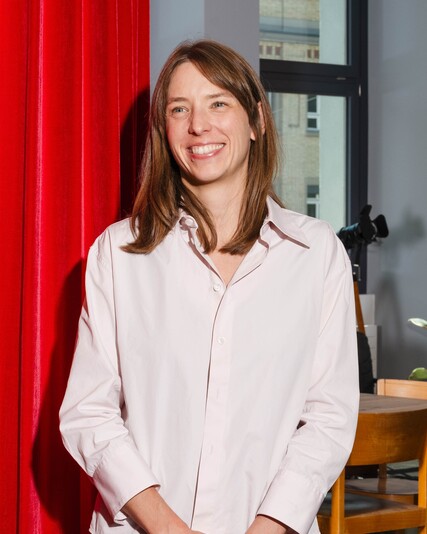 Lena Thomaka stands smiling in front of a red curtain.