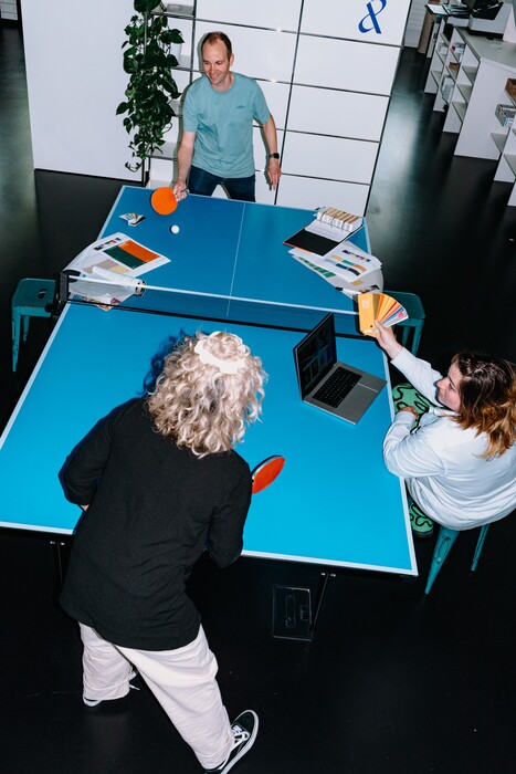 Three team members stand at a table-tennis table with colour swatches and paddles.
