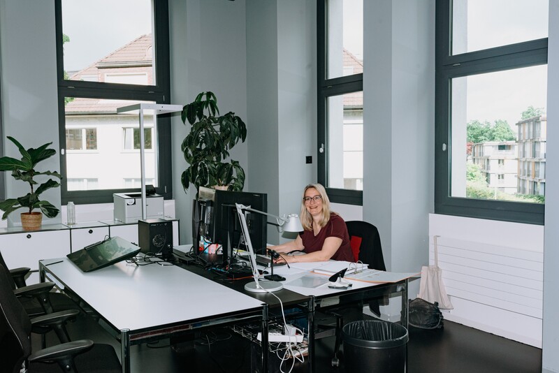 A colleague works alone at a large desk by the window.