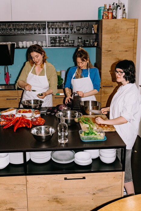 Three colleagues prepare vegetables together in the office kitchen.