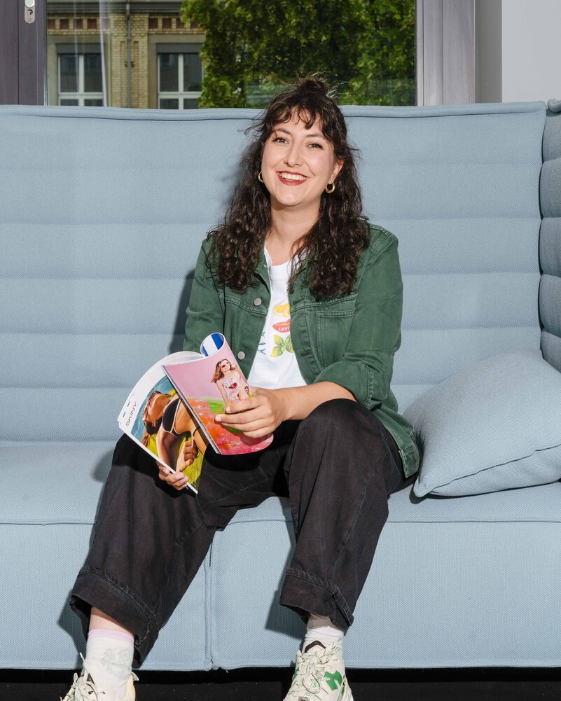 Alisa Kuratli sits on a light-blue sofa holding an open magazine.