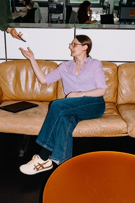 A colleague sits on a leather sofa and reaches for a pen.