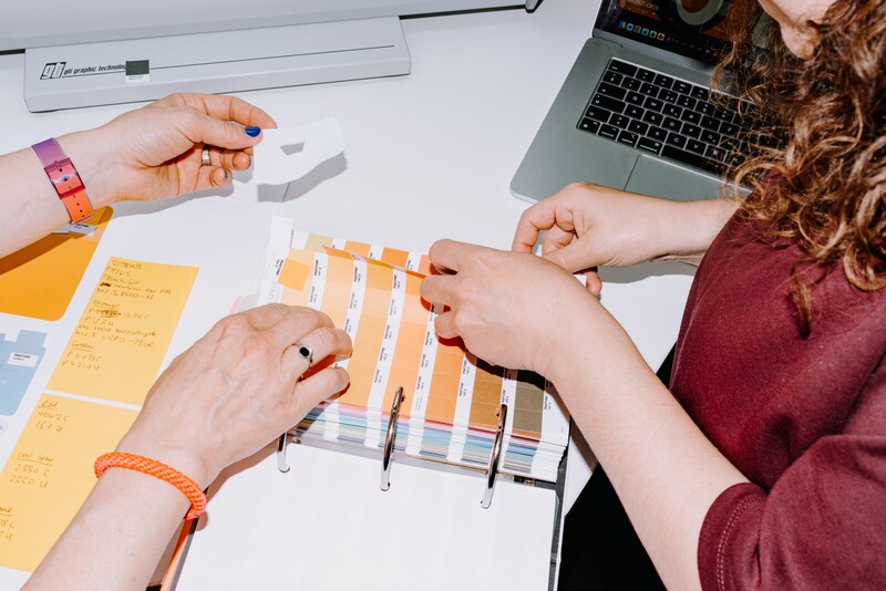 Several hands arrange colour and material samples on a desk.