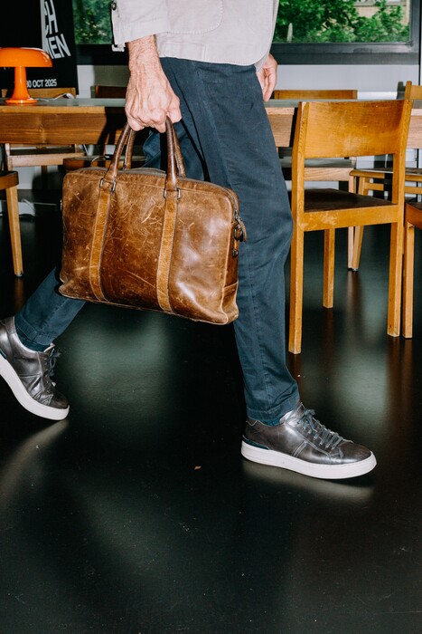 A walking person carries a brown leather briefcase.